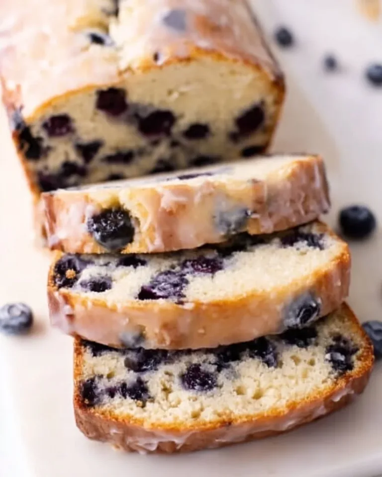 Sliced homemade blueberry bread with fresh blueberries on a wooden table.